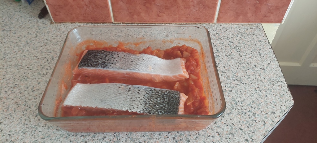 Two salmon steaks on top of the sauce in a microwaveable dish